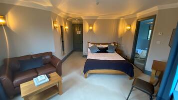 A hotel room with a bed, a brown leather sofa, a wooden coffee table, and a small wooden chair.