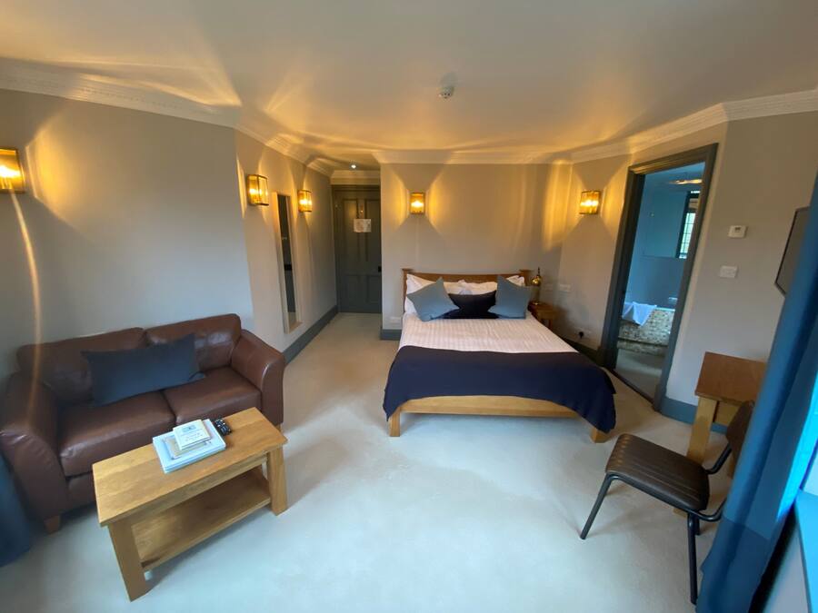 A hotel room with a bed, a brown leather sofa, a wooden coffee table, and a small wooden chair.