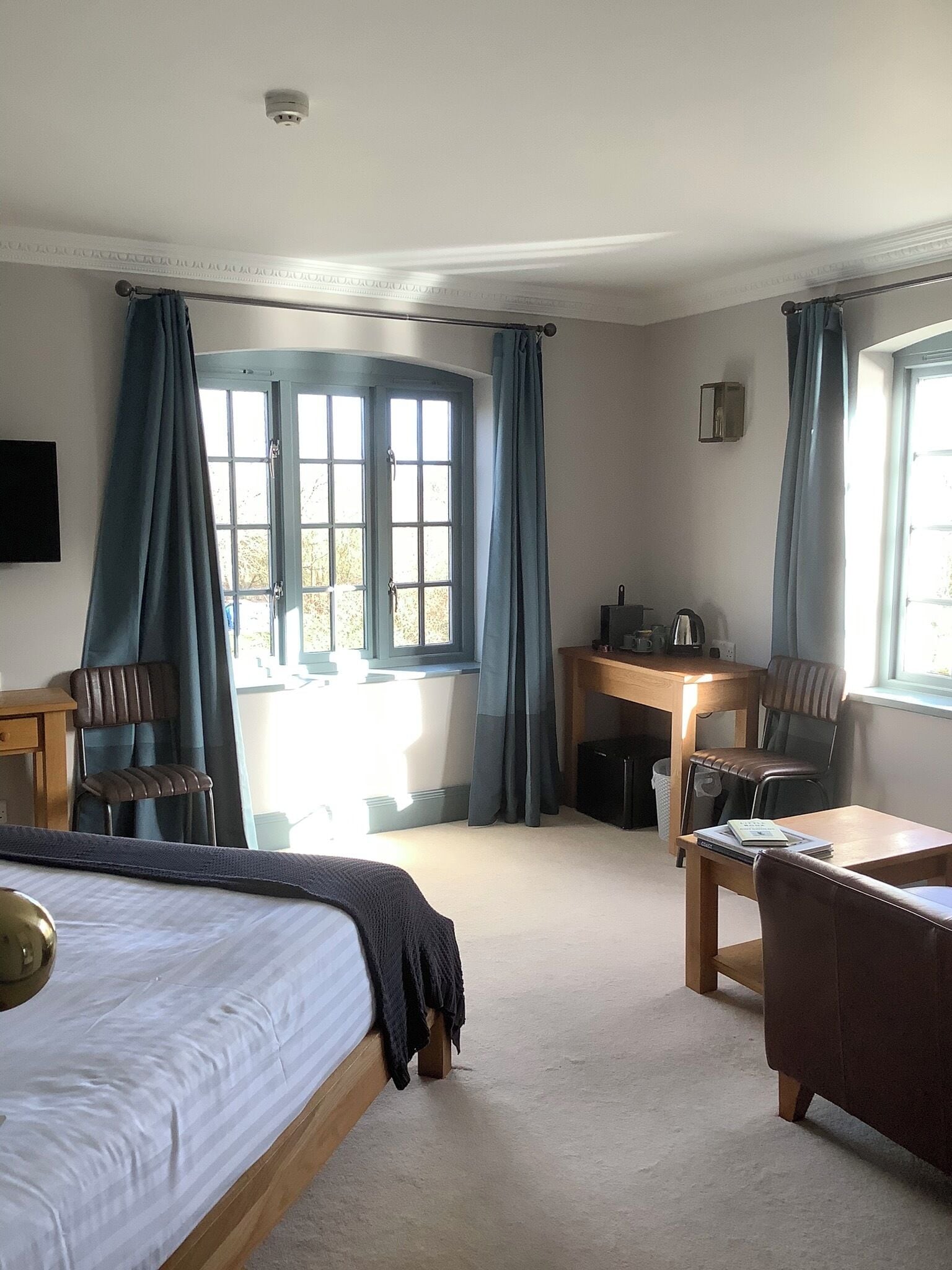 A hotel room with a bed, a desk, two chairs, a small table, and a window with curtains.