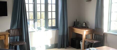 A hotel room with a bed, a desk, two chairs, a small table, and a window with curtains.