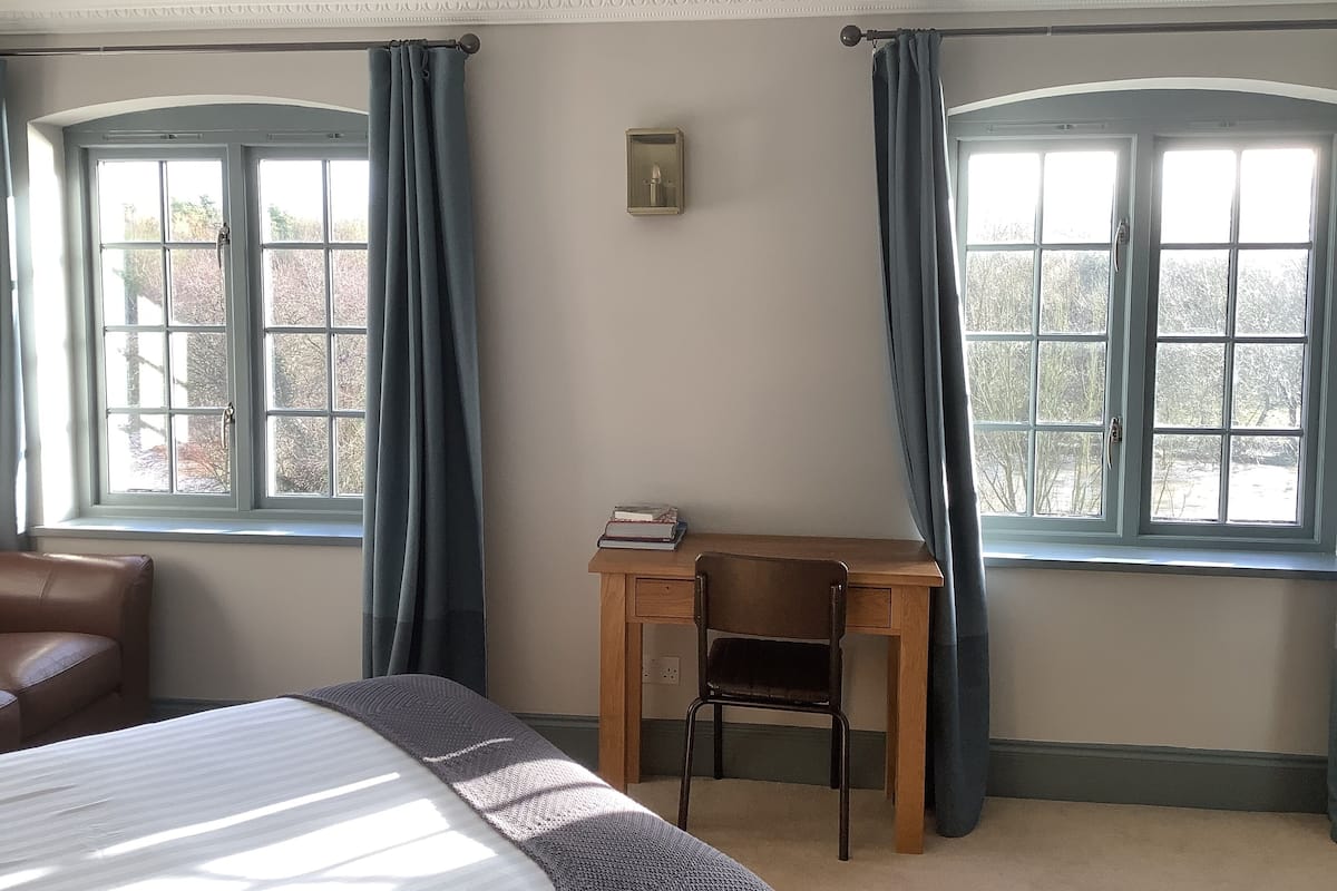 Une chambre avec un lit, un bureau et deux fenêtres avec des rideaux.