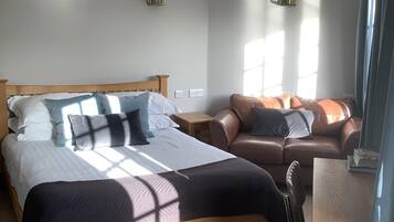 Quarto bem iluminado com uma cama grande, um sofá de couro e uma pequena mesa.