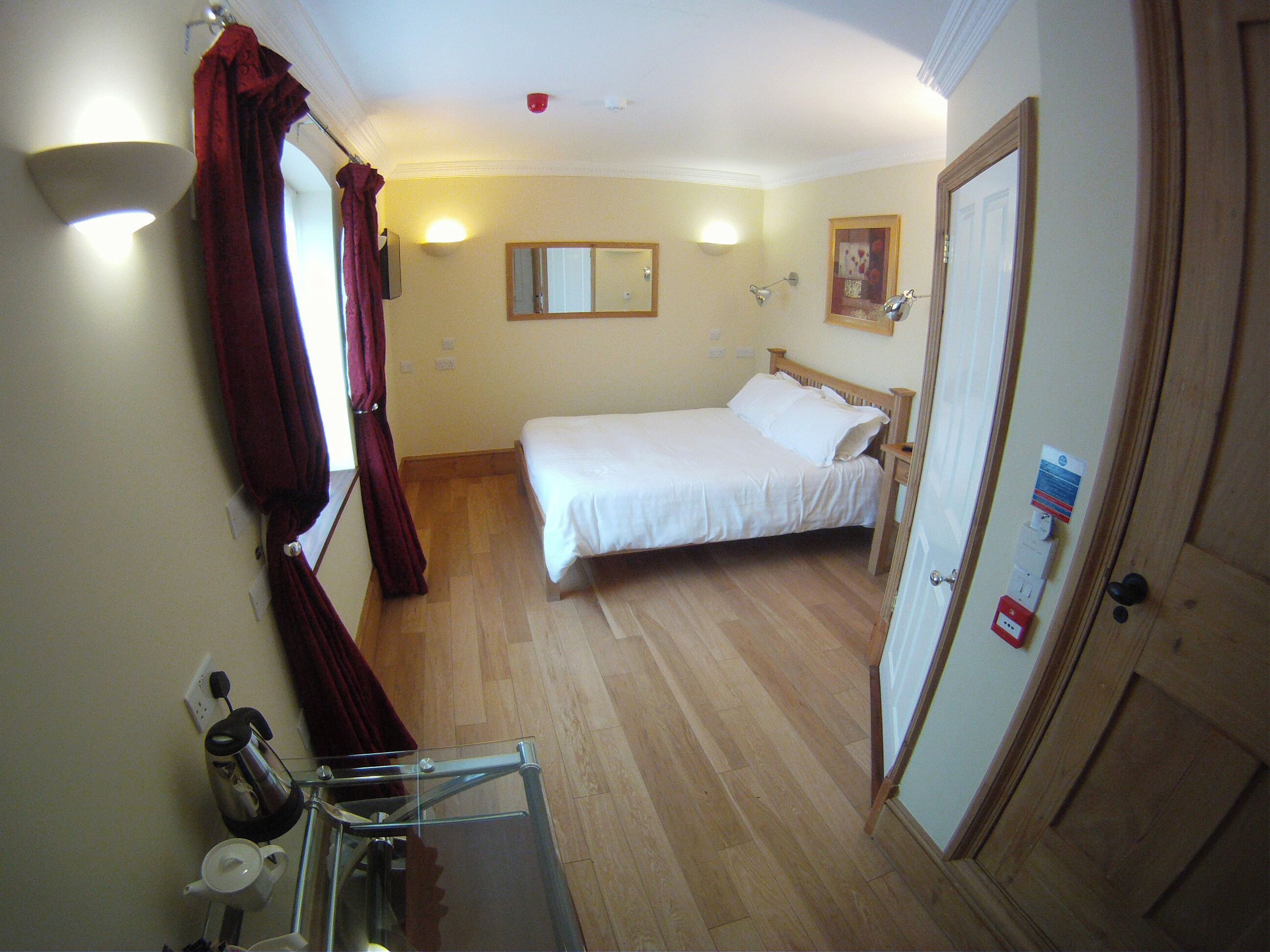 Une chambre d’hôtel avec un lit, une table de chevet, un miroir, un rideau rouge et une porte.