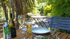A wooden table with a bottle of Peroni Nastro Azzurro, a glass of white wine, and a plate of food including prosciutto, cheese, and a salad. - The Mooringpost (Gloucester)
