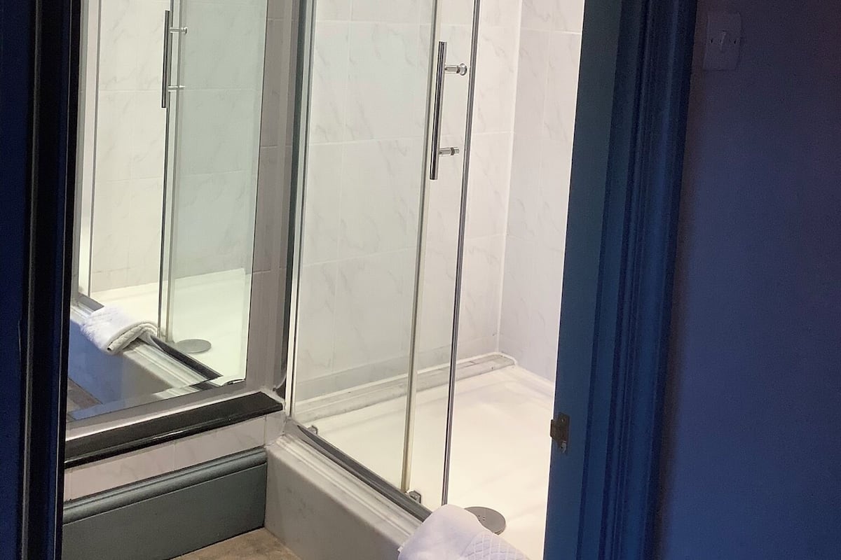 Une douche fermée par des parois de verre, avec un mur recouvert de carreaux blancs et une serviette visible sur le sol.