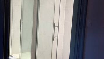A glass-enclosed shower with a white tiled wall and a visible towel on the floor.