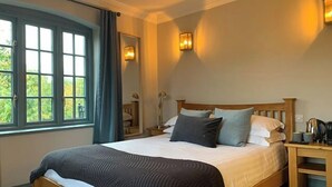 A bedroom with a wooden bed, a nightstand, a lamp, and a window with curtains. - The Mooringpost (Gloucester)