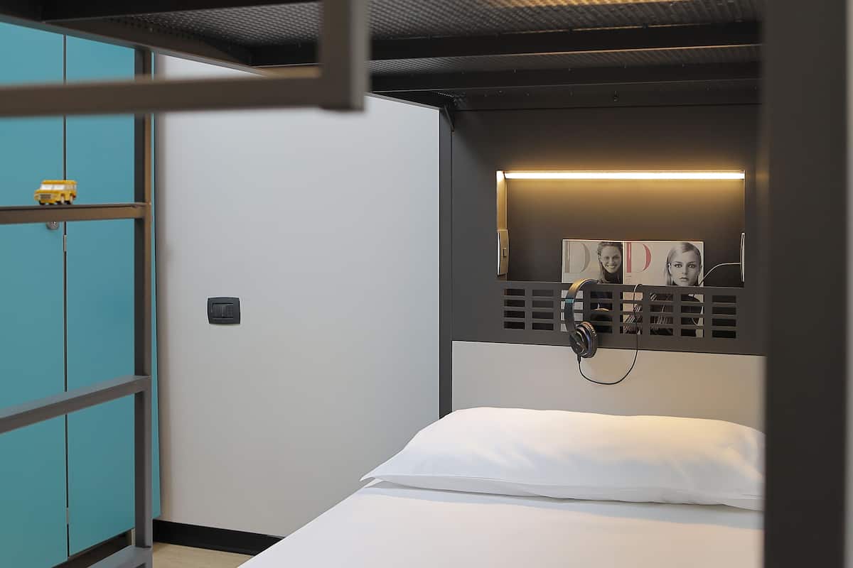 Una cama litera con colchón y almohada blancos, un estante pequeño con un juguete y un teléfono instalado en la pared.