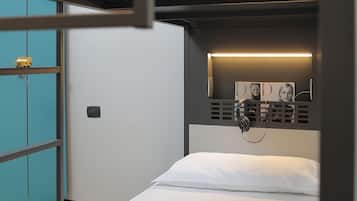 Una cama litera con colchón y almohada blancos, un estante pequeño con un juguete y un teléfono instalado en la pared.