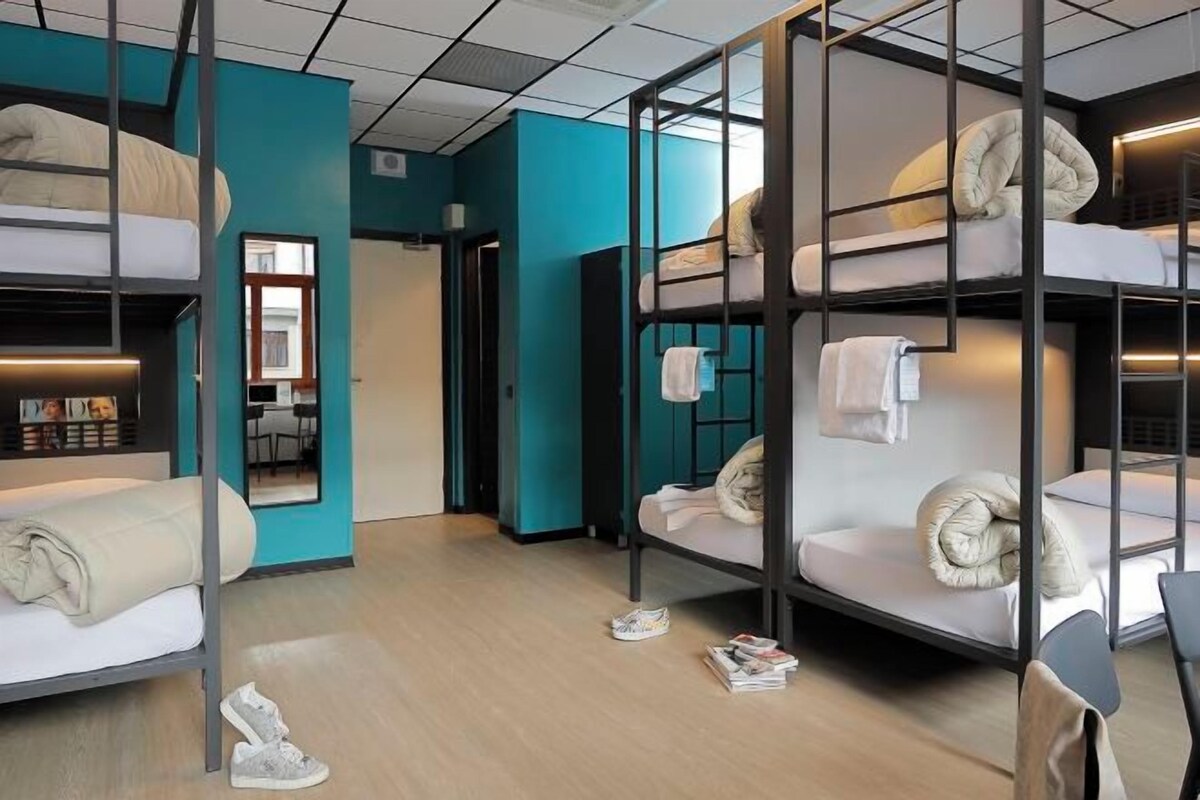 A bunk bed room with a teal accent wall, a mirror, and a small seating area with a table.