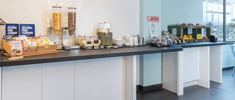 A breakfast bar with labeled containers of cereals, coffee machines, and a fruit display.