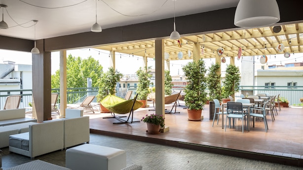 A covered outdoor seating area with wicker furniture, potted plants, and hanging pendant lights.
