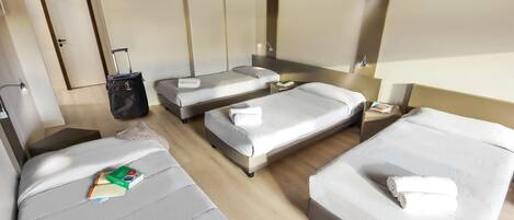 Ein Hotelzimmer mit zwei Einzelbetten, einer Schlafcouch, einem Schreibtisch, einem Fernseher und einem Koffer.