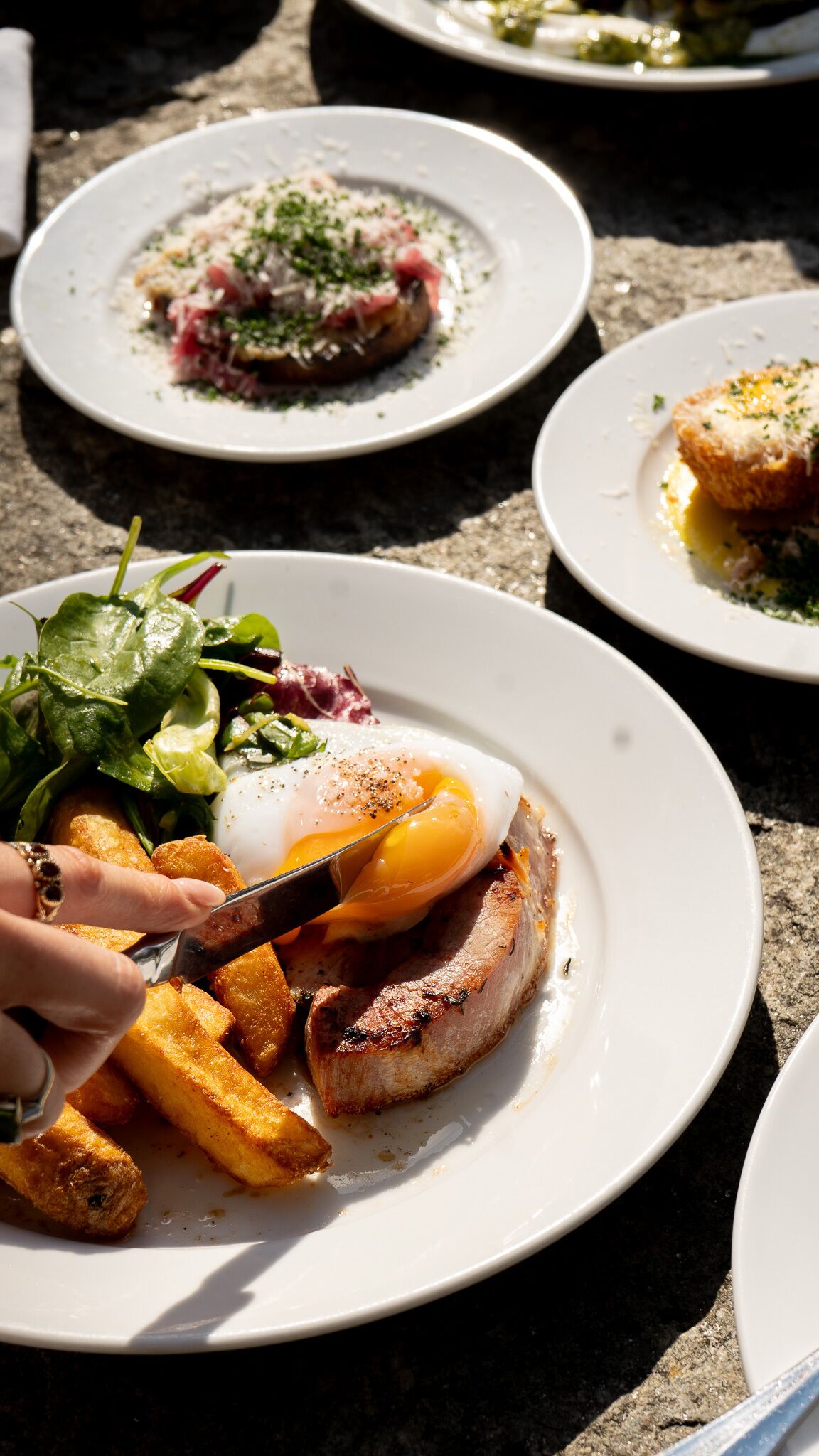 A dining table with plates of food, including a dish with a poached egg, greens, and fries.