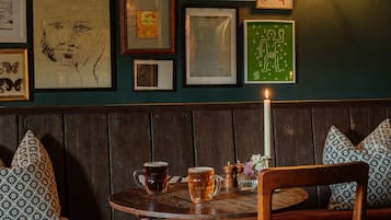 A cozy interior with a wooden bench, a table with a candle, and various framed artworks on the wall.