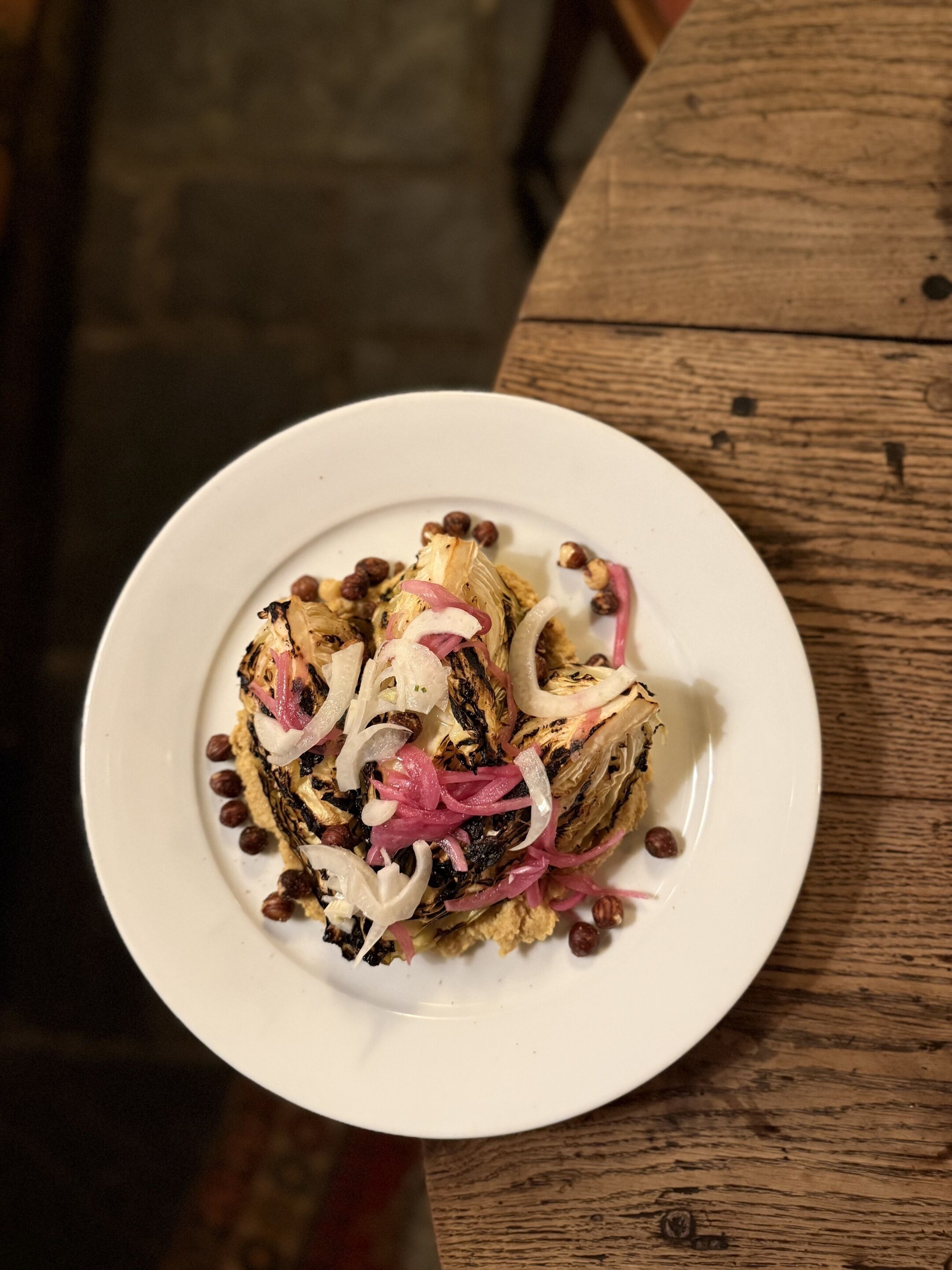 A plate of food with grilled vegetables and nuts on a white plate, placed on a wooden table.