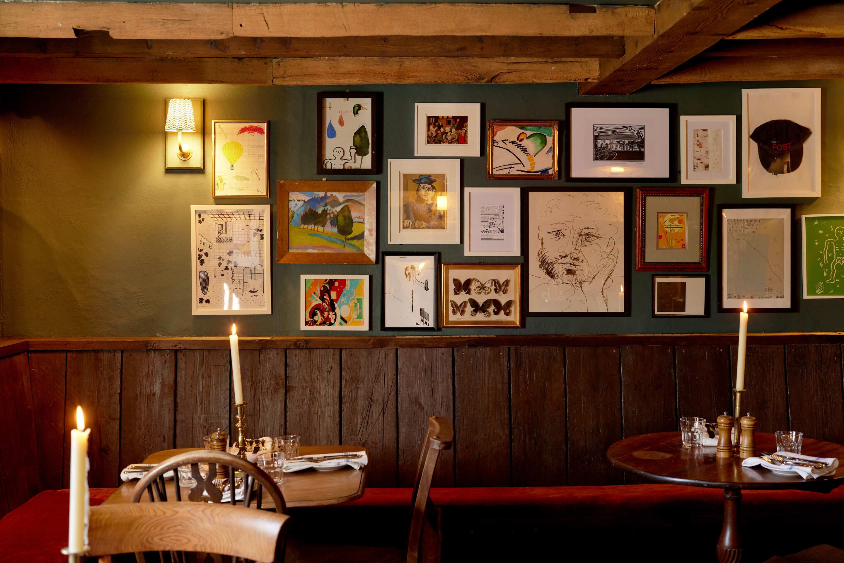 A restaurant interior with wooden paneling, a wall adorned with framed artwork, and a table set with candles and glasses.