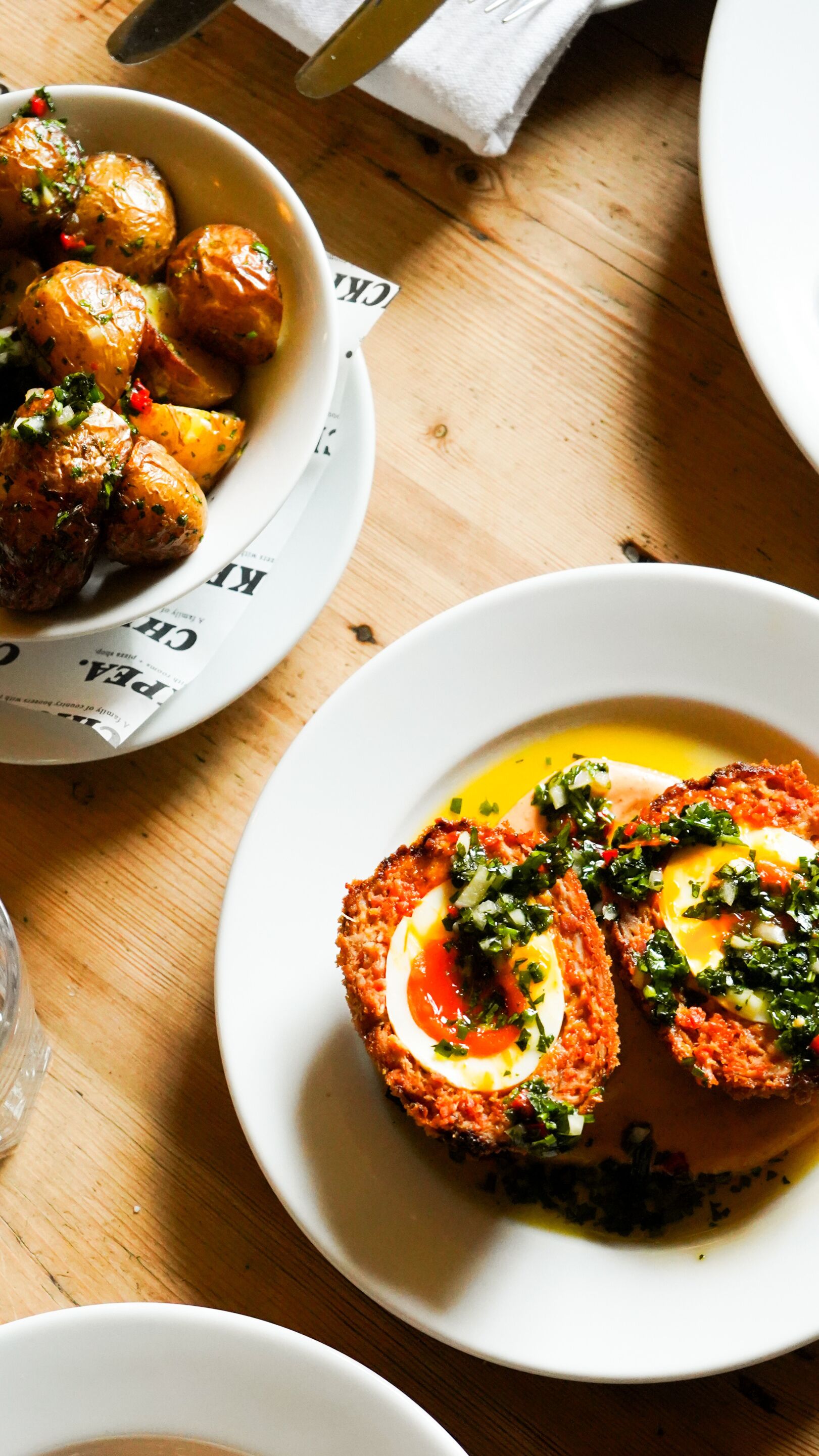 A table with dishes including roasted potatoes and a breaded egg dish.