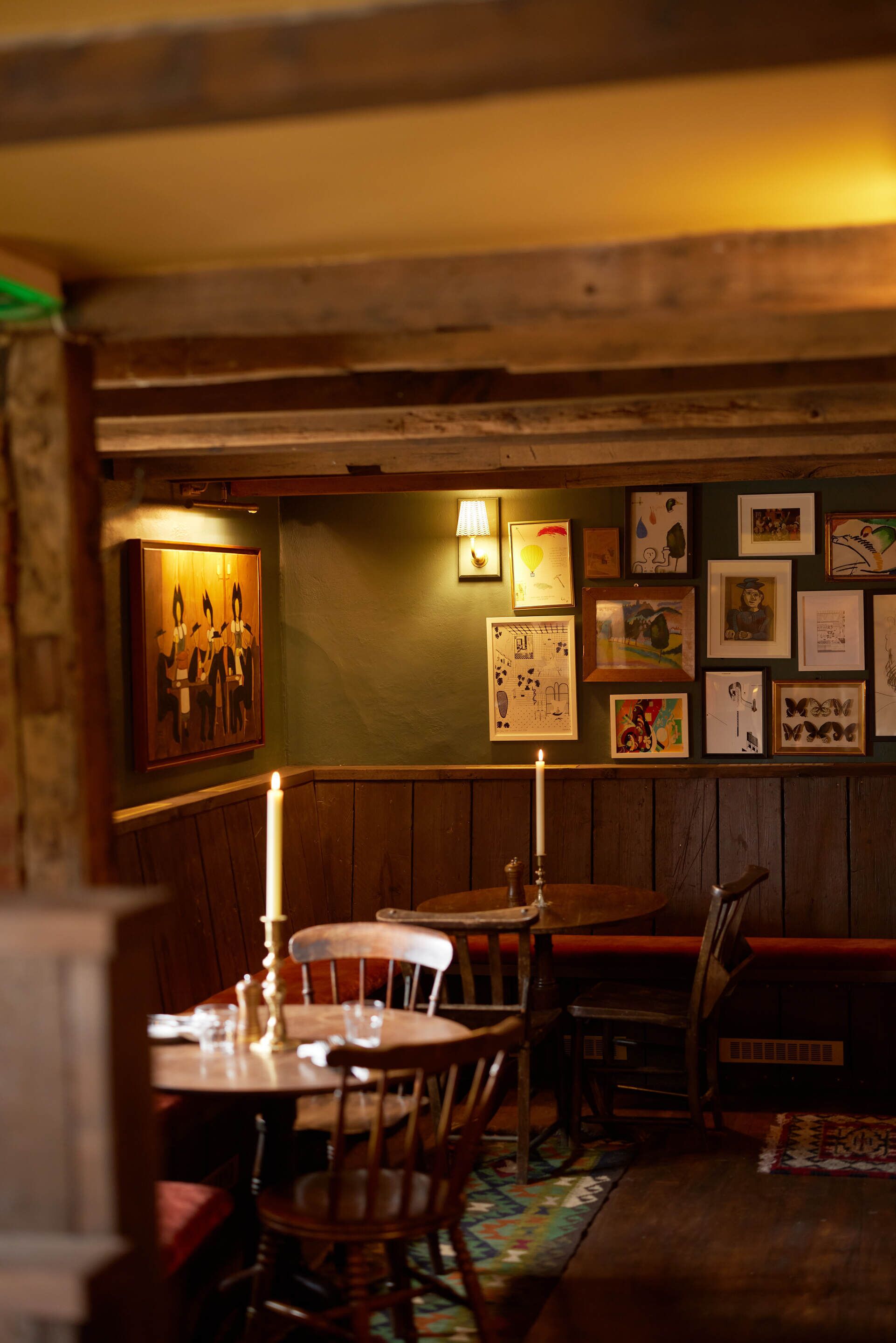 A dimly lit dining area with wooden furniture, a candle on the table, and artwork on the wall.