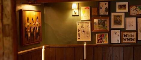 A dimly lit dining area with wooden furniture, a candle on the table, and artwork on the wall.