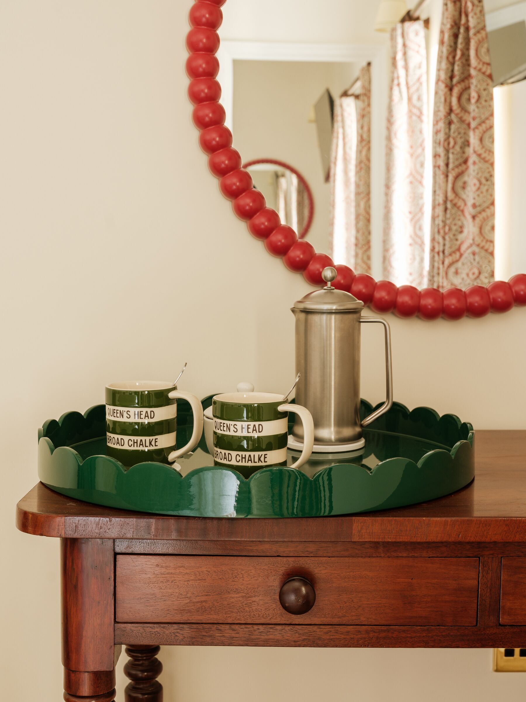 Una mesa de madera con una bandeja verde que sostiene una tetera y dos tazas con la etiqueta 'Queen's Head Broad Chalke'.