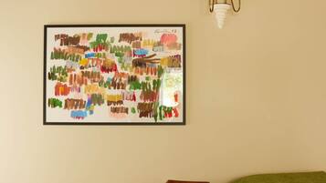 Una habitación con una silla de madera, una cama verde, una lámpara de pared y un cuadro abstracto colorido.