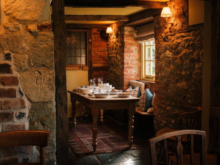 Un comedor rústico con una mesa de madera dispuesta para una comida, paredes de piedra y un ventanal con luz natural.