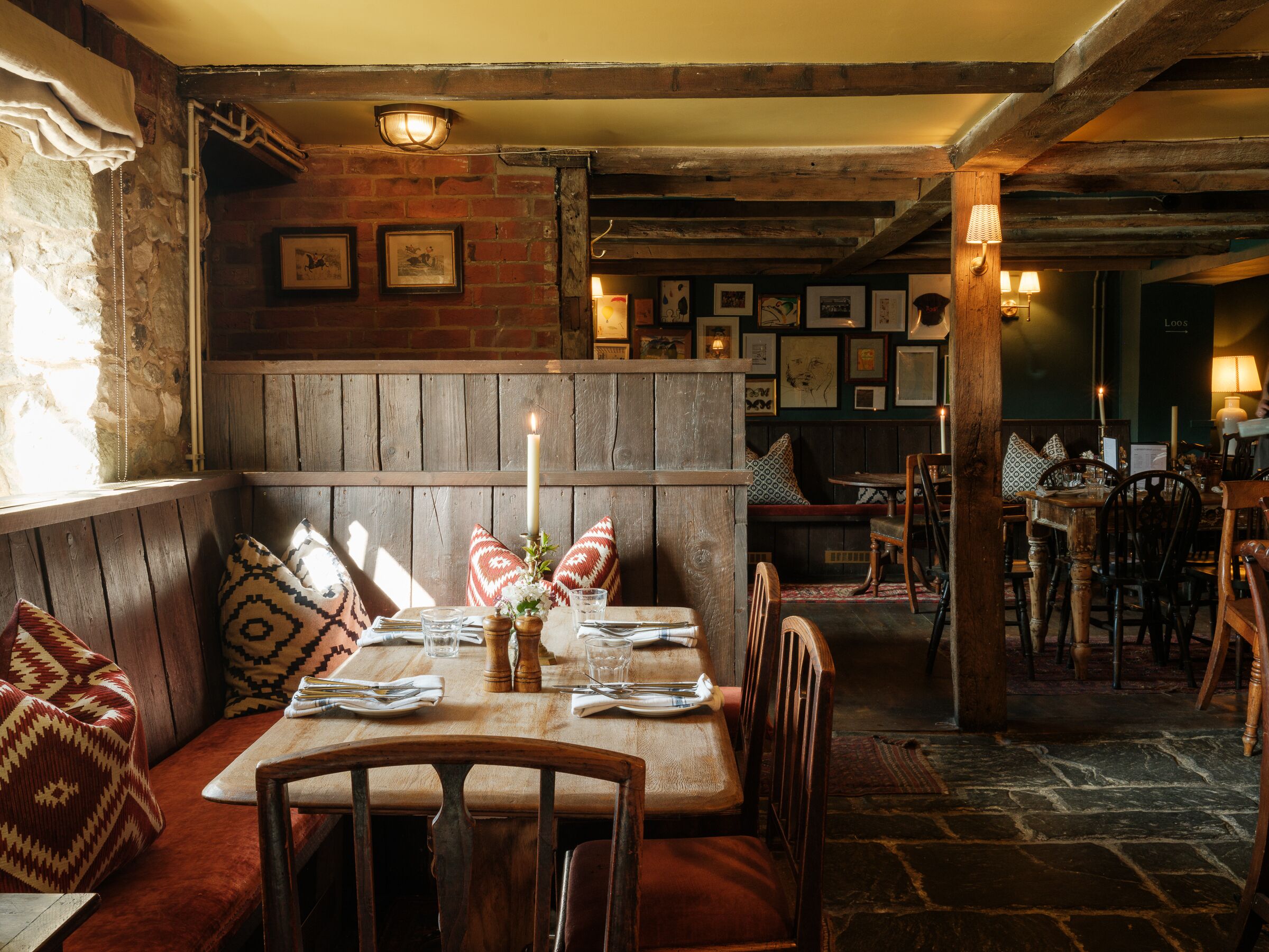 A rustic dining area with wooden benches, a table set for two, and a brick wall with framed pictures.