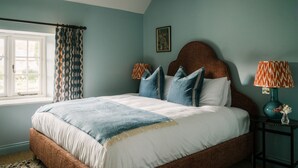 Une chambre à coucher avec un grand lit, une fenêtre avec des rideaux, une table de chevet avec une lampe et un tableau accroché au mur.