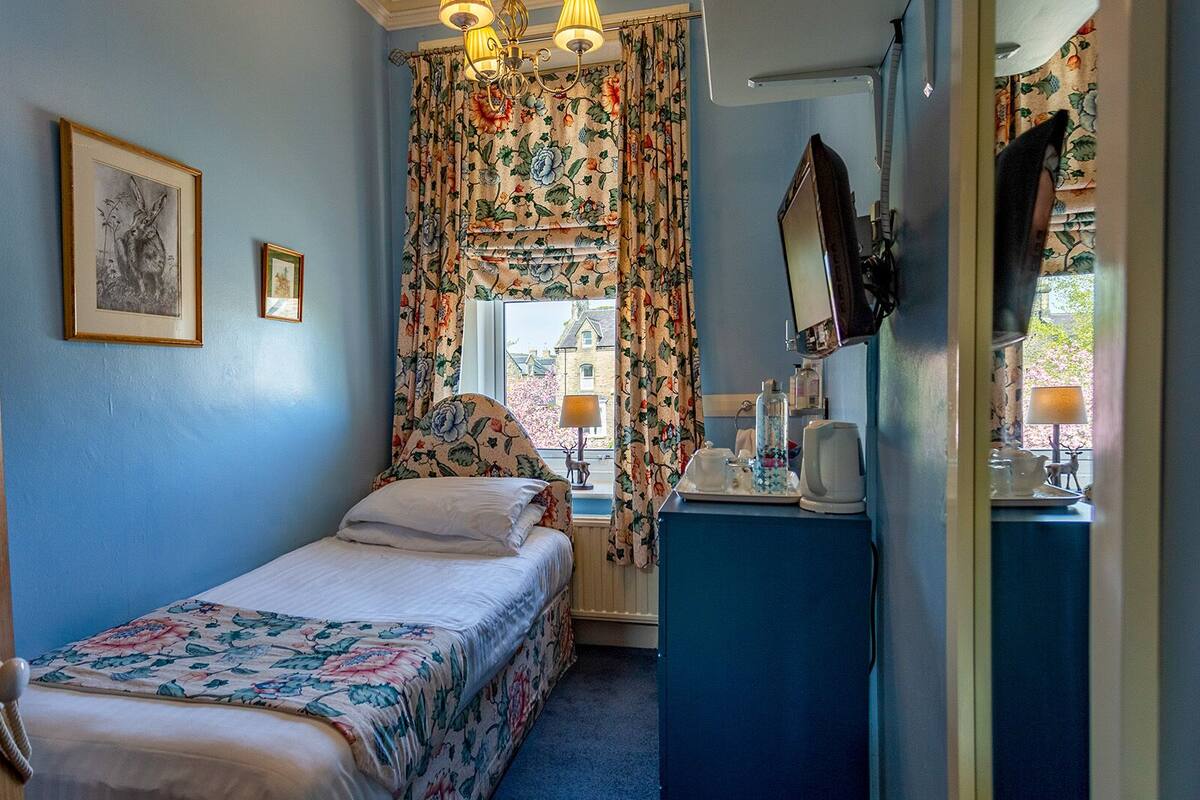 Un dormitorio con cama, cómoda, espejo y ventana con cortinas florales.