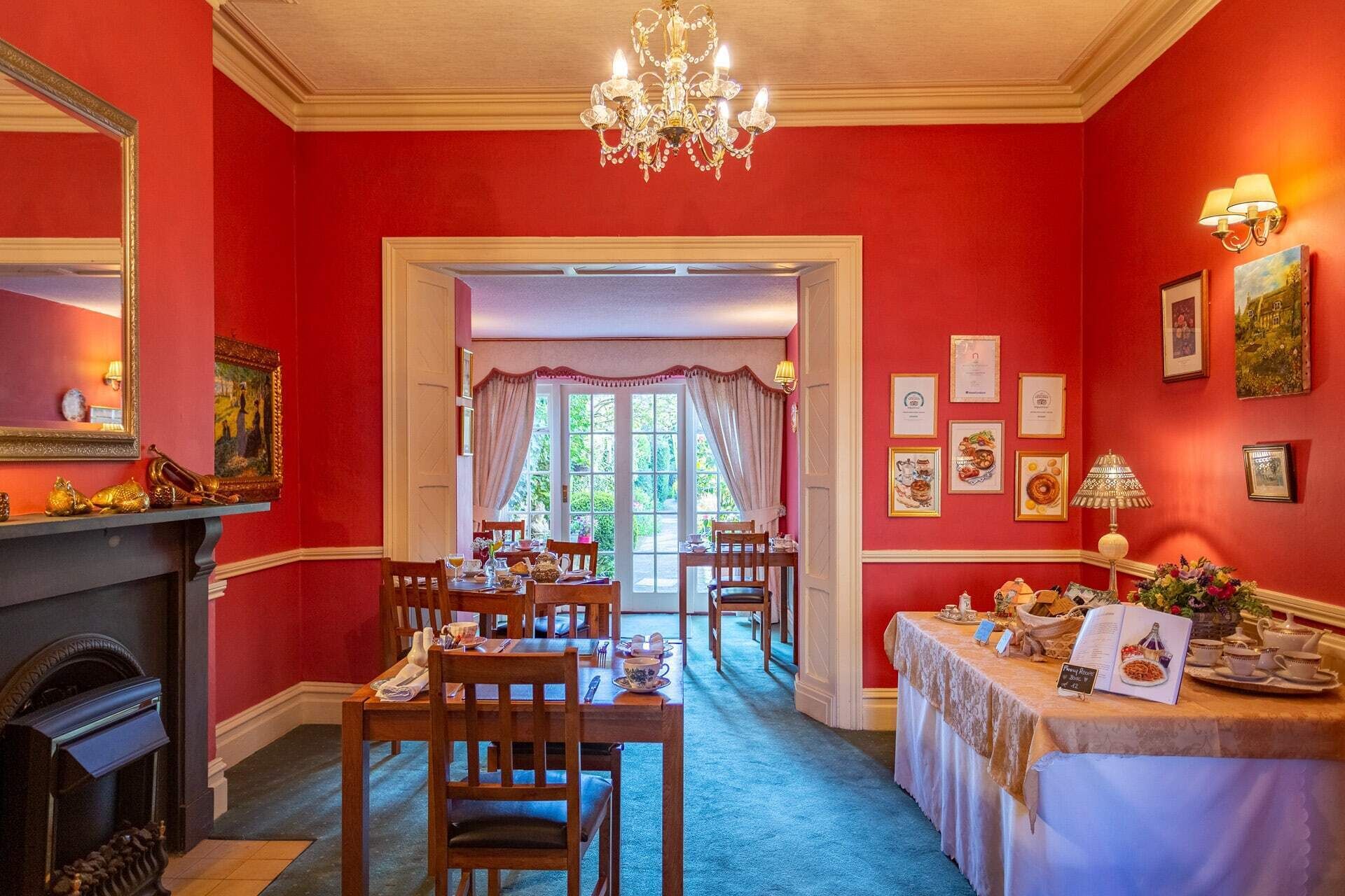Un comedor con pared roja, un candelabro y una mesa dispuesta para tomar té.