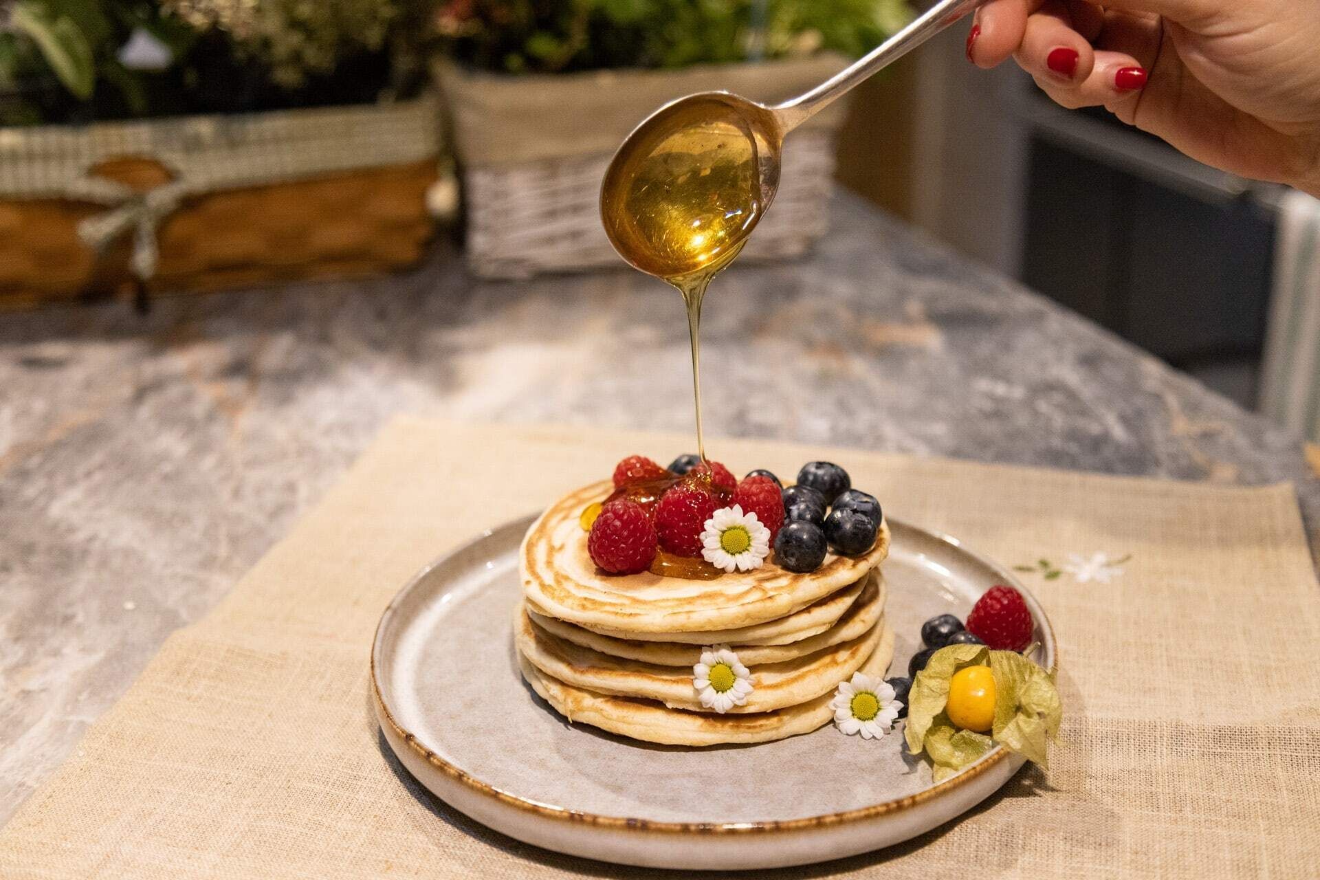 Une pile de crêpes arrosées de sirop, accompagnée de fruits rouges frais et d’une petite fleur.