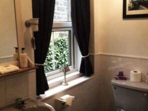 A bathroom with a window, a sink, a mirror, a toilet, and a towel rack. - Homelands Guest House (Barnard Castle)