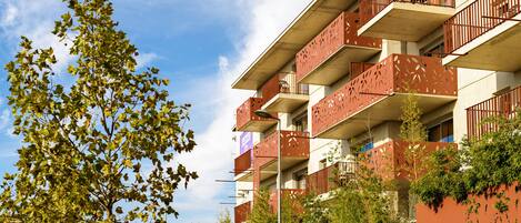 A multi-story building with balconies, surrounded by trees and greenery.