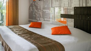 Habitación de hotel con una cama grande, dos almohadas naranjas, un cabecero y un mural de un edificio clásico en la pared.