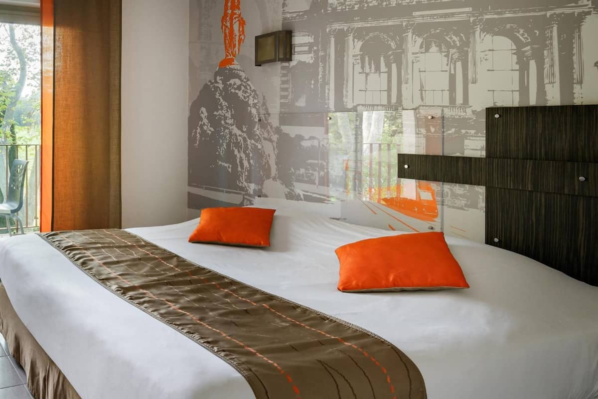 Habitación de hotel con una cama grande, dos almohadas naranjas, un cabecero y un mural de un edificio clásico en la pared.