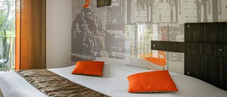 A hotel room with a large bed, two orange pillows, a headboard, and a mural of a classical building on the wall.