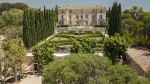 Un edificio grande e histórico con una fachada simétrica, un jardín formal y una escalera central que conduce a la entrada.