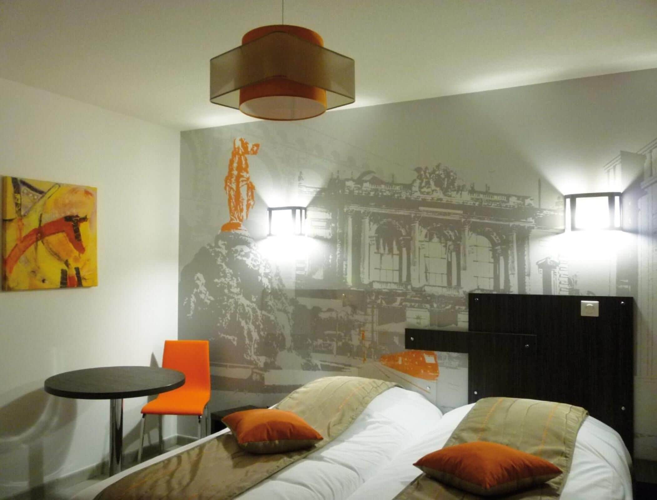 A hotel room with a bed, a chair, a small table, and a wall with a mural.