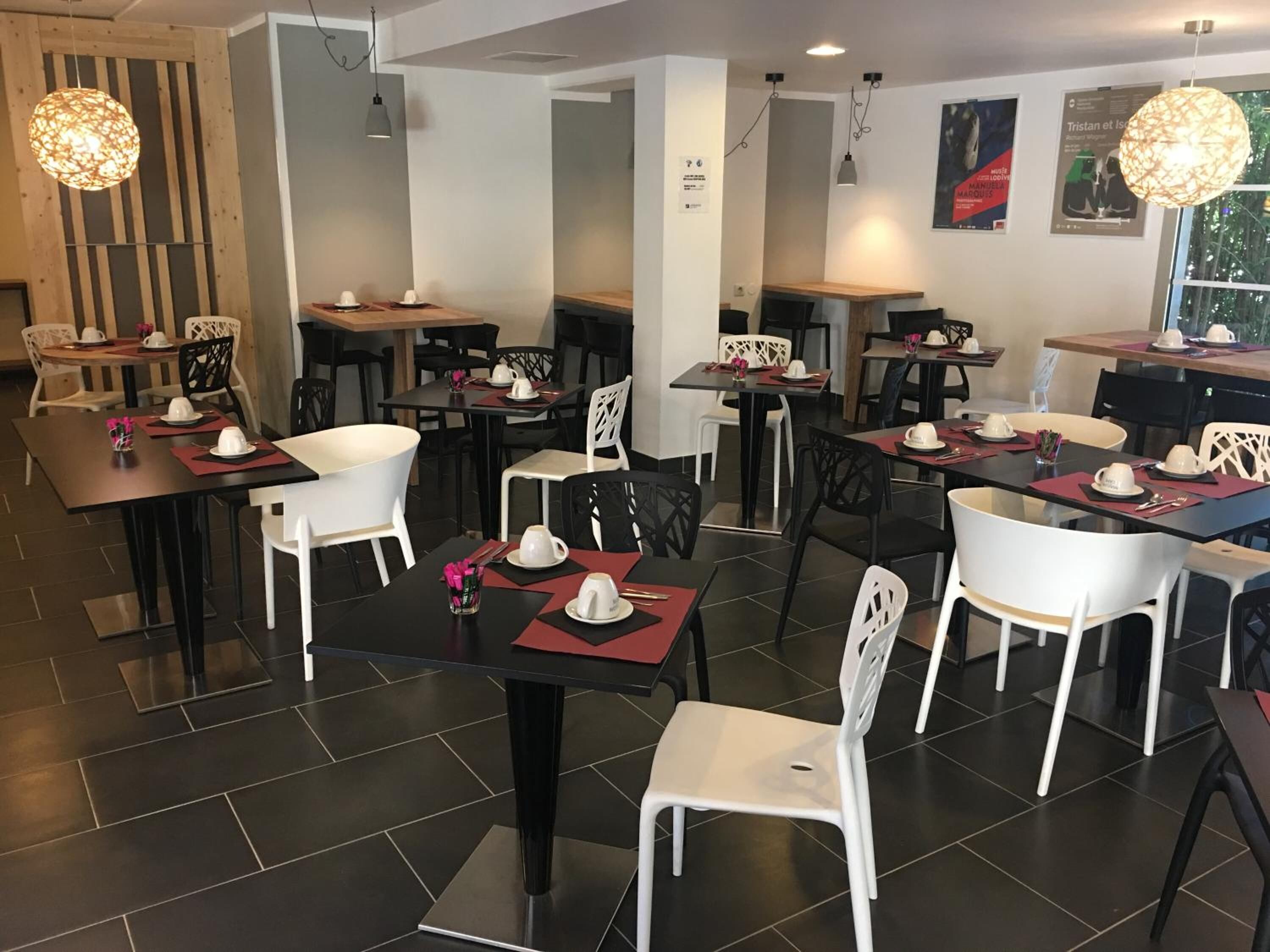 Un espace de restauration moderne avec des tables prévues pour deux personnes, agrémenté de chaises blanches et de tables noires.