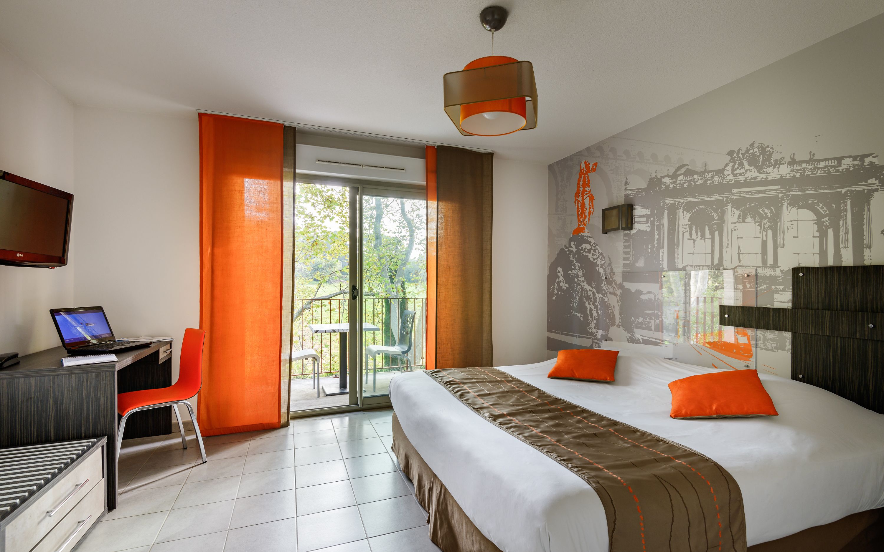 Een hotelkamer met een bed, een bureau met een laptop, een stoel en een groot raam met gordijnen.