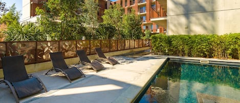 A pool area with lounge chairs and a clear view of a multi-story building in the background.