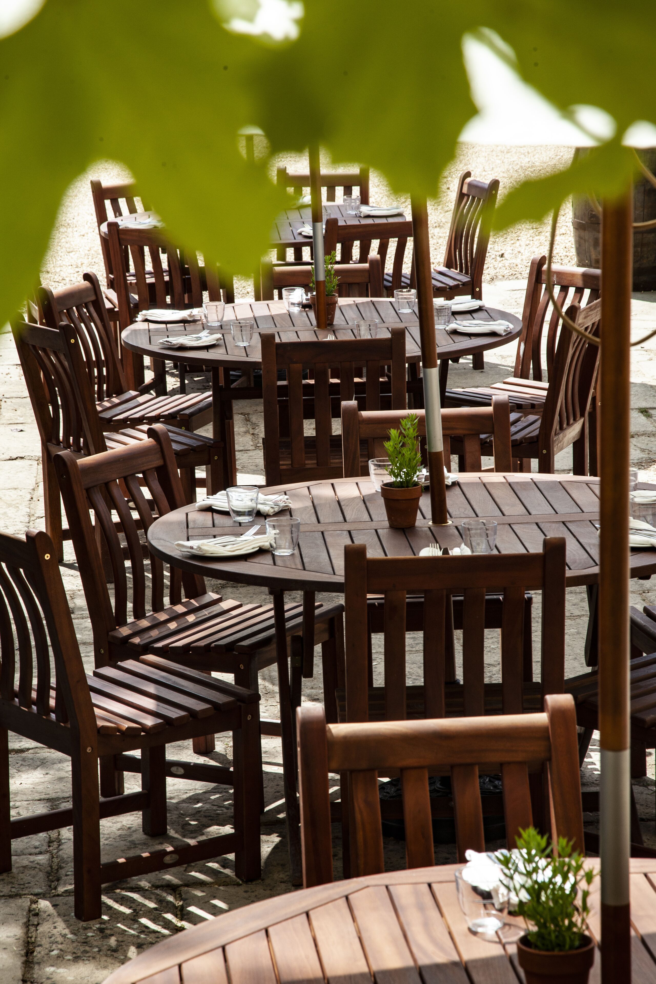 A patio area with wooden tables and chairs, some with potted plants.