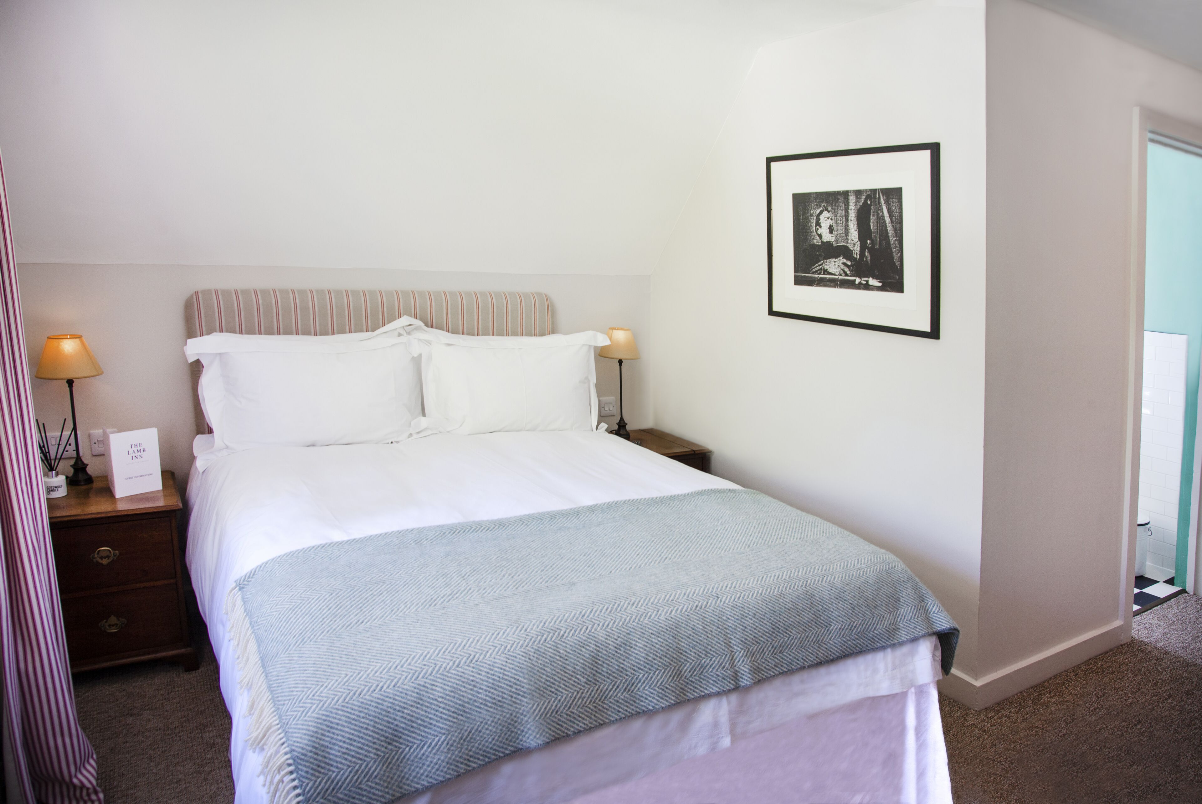 Ein ordentlich bezogenes Bett mit einem gestreiften Kopfteil, zwei Nachttischlampen und einem gerahmten Bild an der Wand.