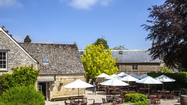 A stone building with outdoor seating and umbrellas. - The Lamb Inn (Chipping Norton)