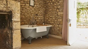 A bathroom with a stone wall, a clawfoot bathtub, and a wooden door. - The Lamb Inn (Chipping Norton)