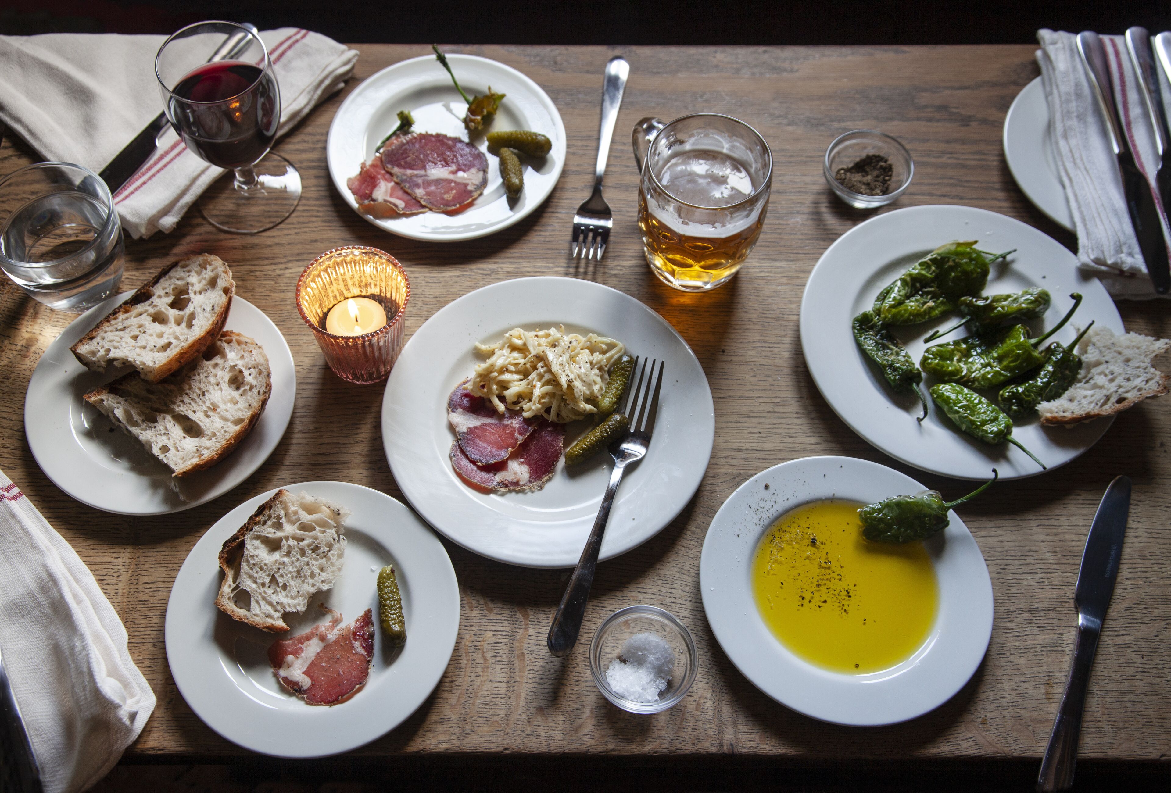 A wooden table with plates of food, including bread, pasta, and soup, and glasses of wine.