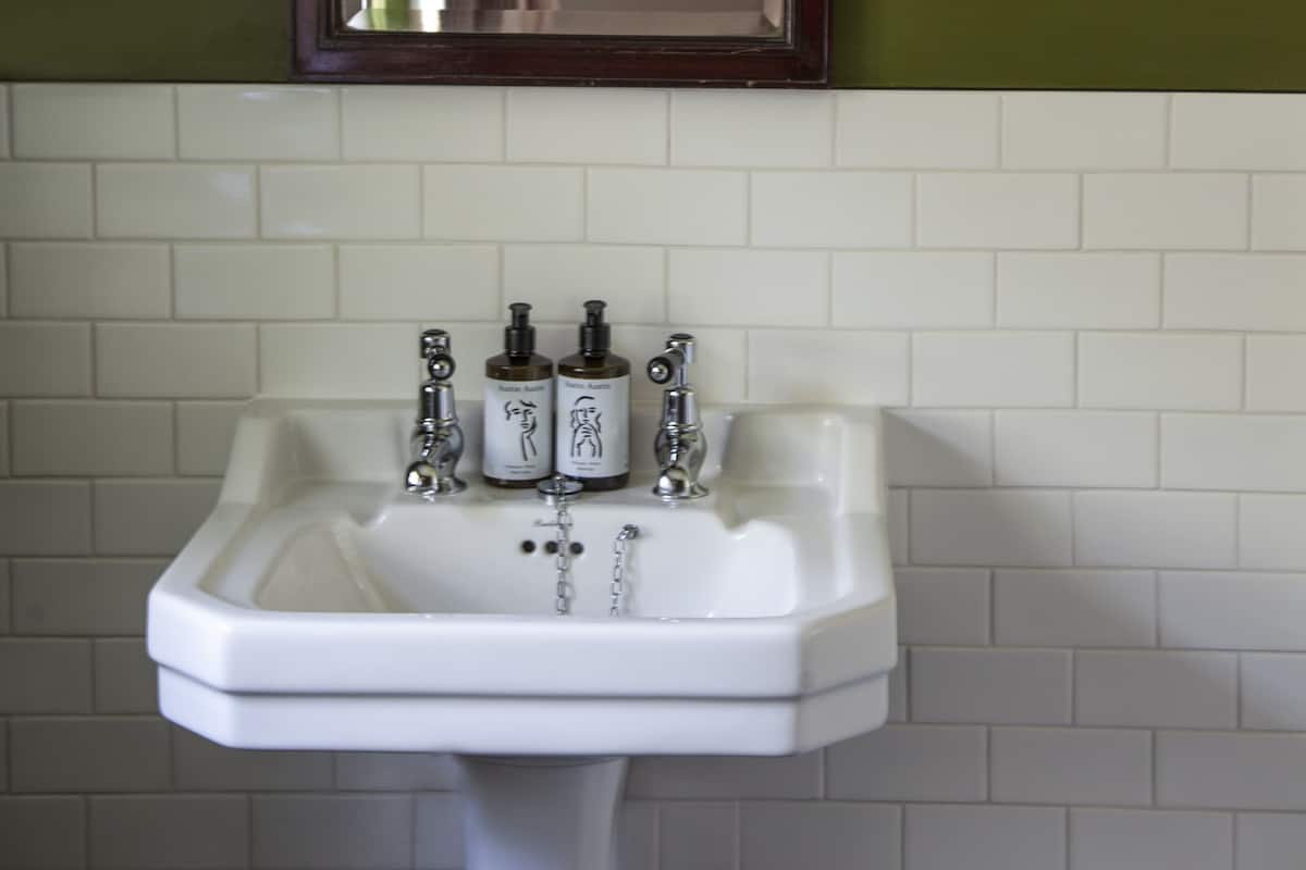 A bathroom with a white sink, green walls, and a mirror with two wall-mounted lights.