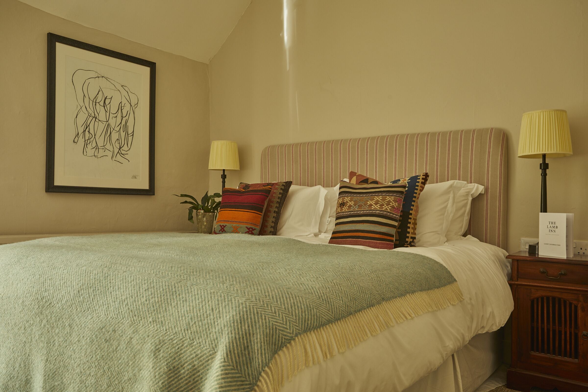 A neatly made bed with a striped headboard, two bedside lamps, and a framed artwork on the wall.