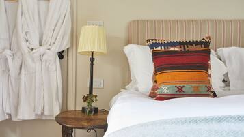 A hotel room with a bed, a bedside table with a lamp, a vase with flowers, and two white bathrobes hanging on a rack.